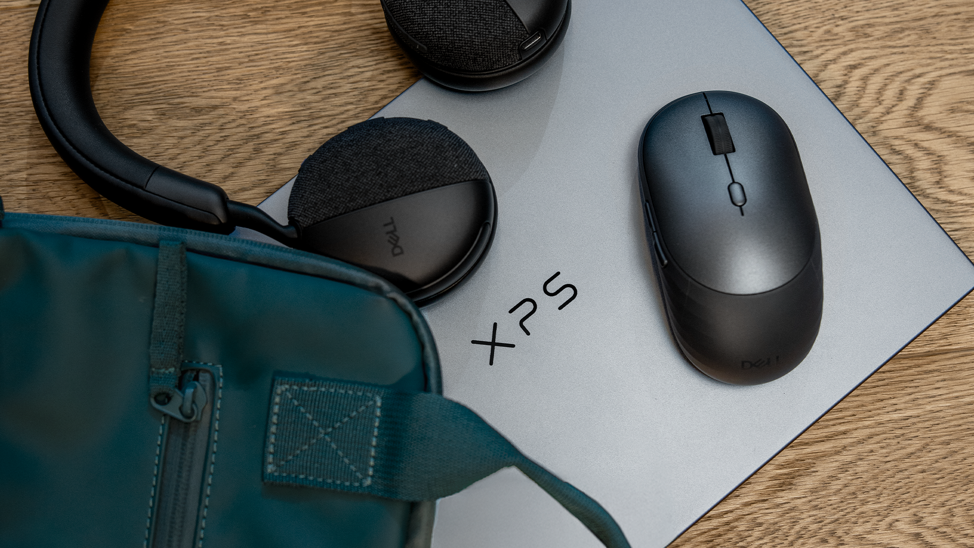 Dell XPS 13 top-down view, laptop closed, with a backpack next to it and a mouse and headphones on top